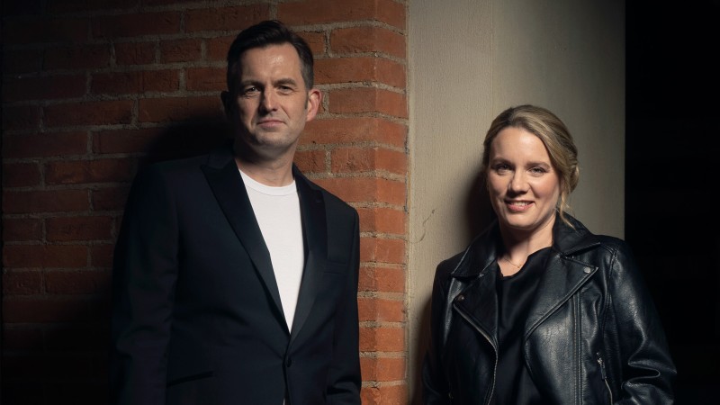 Chrsitian Forshaw and Grace Davidson smiling to the camera stood in front of a brick wall