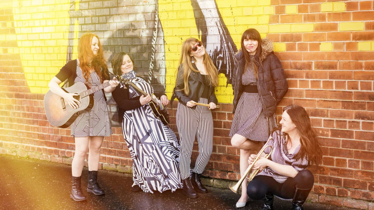 The five members of Wookalily standing with instruments in front of an exterior wall featuring street art.