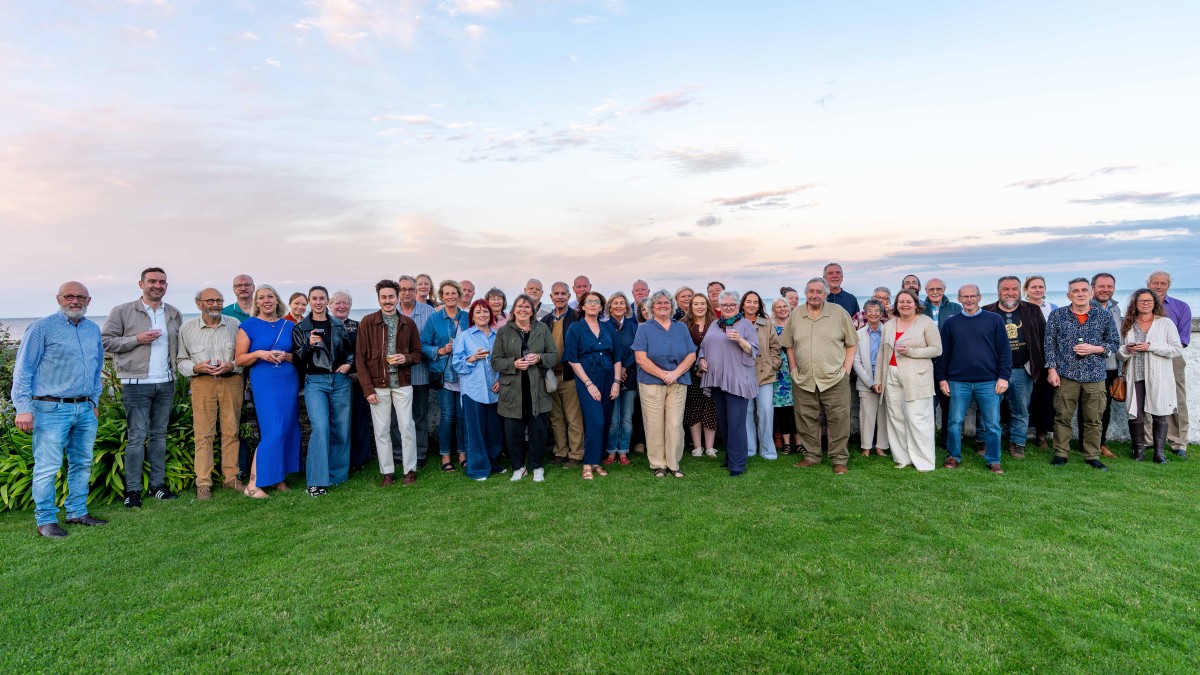 Around 50 members of the Portico volunteer team standing outside on grass with the evening sky above the Irish Sea behind them.