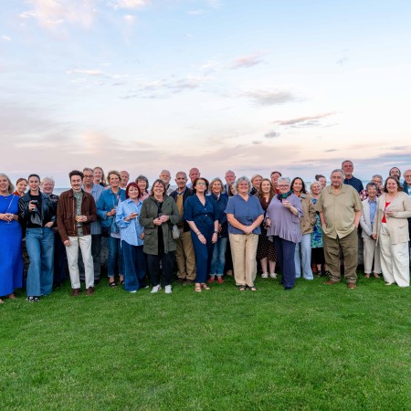 Around 50 members of the Portico volunteer team standing outside on grass with the evening sky above the Irish Sea behind them.